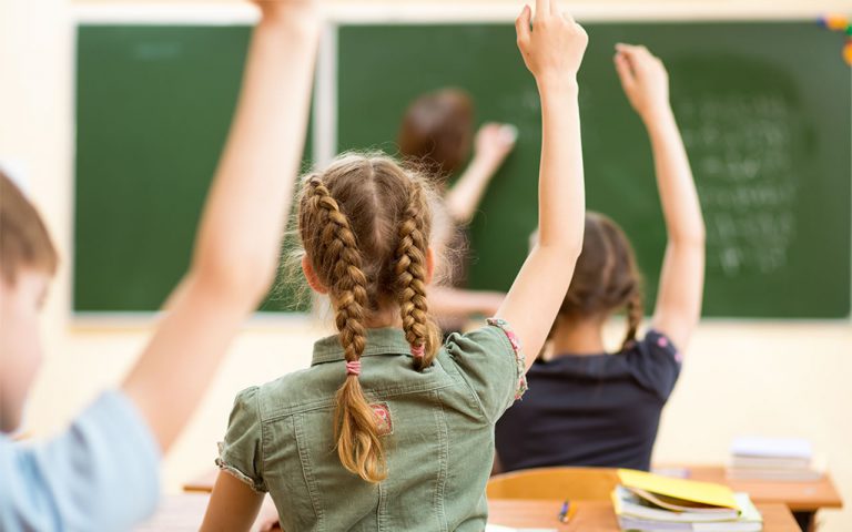 Elementary Kids in classroom raising hands.