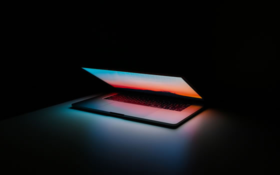 A laptop glows on a desk in a dark room.