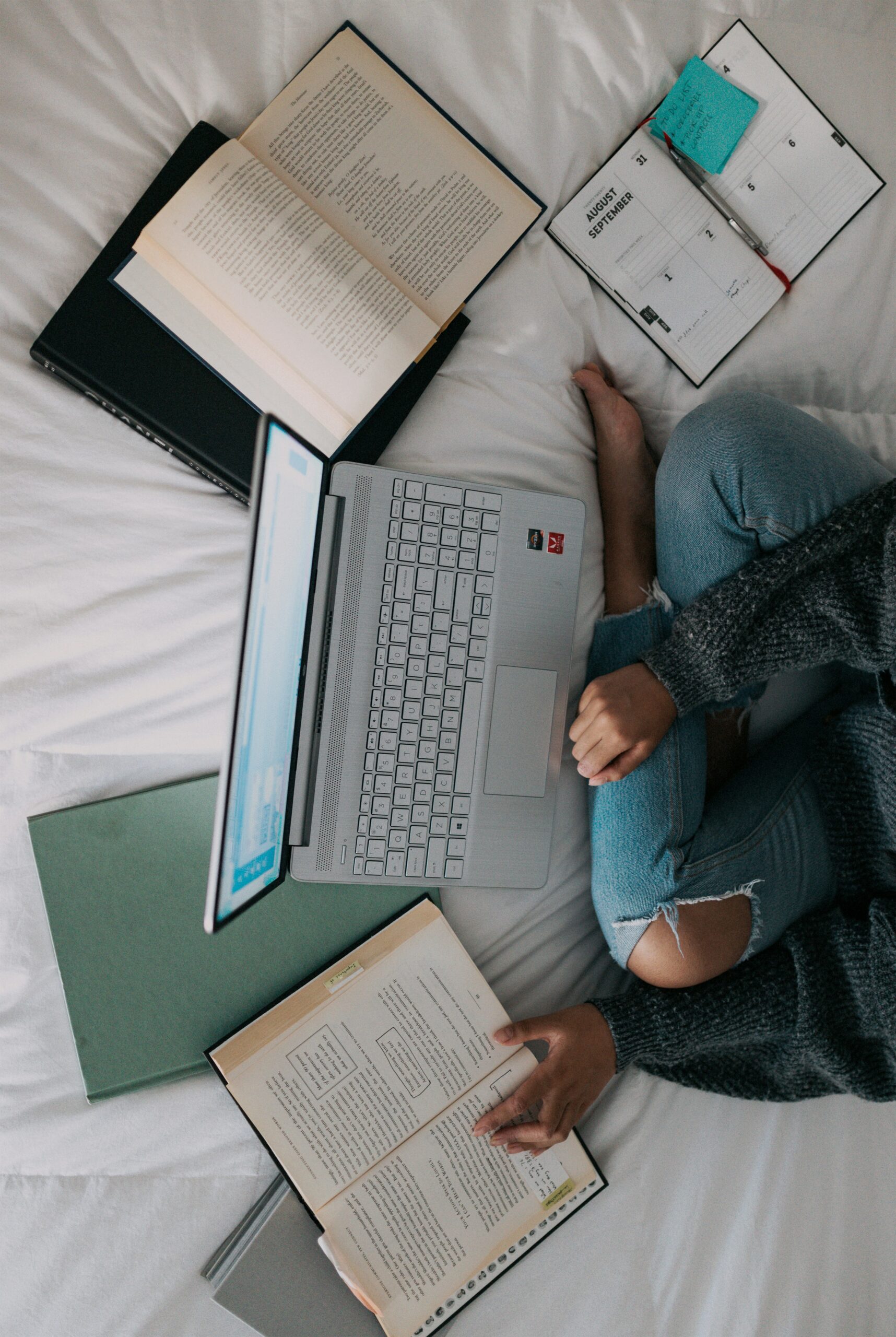 student with their computer and study documents spread across a bed